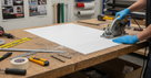 Worker in blue gloves cutting a white PVC sheet with a circular saw on a timber bench, tools laid out