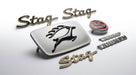 Flat lay of Triumph Stag Mk1 badge set: leaping stag grille badge, script badges and TRIUMPH badge
