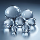 Seven clear acrylic spheres in graduated sizes grouped on a blue-grey reflective surface, highlights on each.