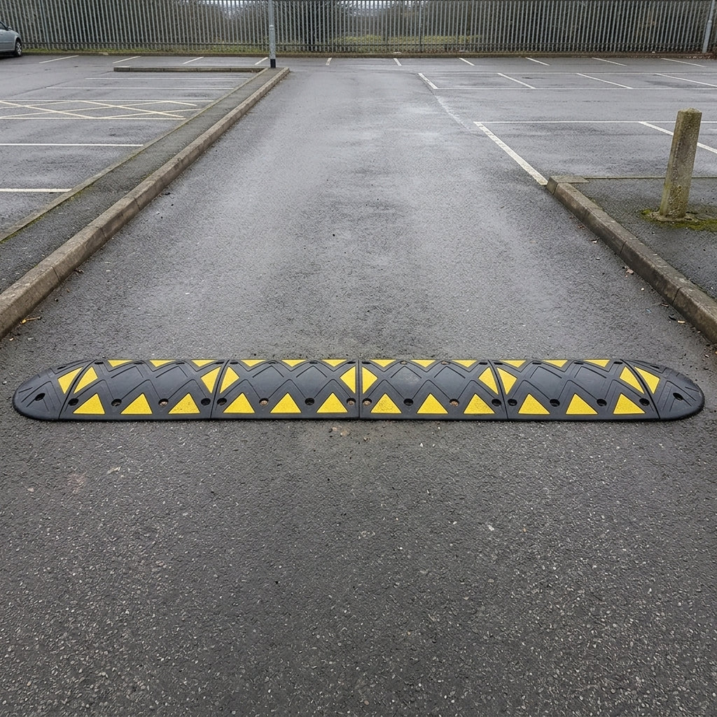 Black rubber speed bump with yellow reflective triangles across a car park entrance lane