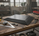 Fanned stack of black fluted plastic sheets on a timber bench, square, tape and knife around them