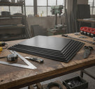 Fanned stack of black fluted plastic sheets on a timber bench, square, tape and knife around them