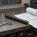 Textured black nylon rod on a steel bench beside vernier callipers and a curled drawing