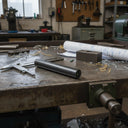Textured black nylon rod on a worn steel bench with callipers, swarf and rolled drawings