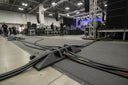 Black ramp sections in use at an indoor event, guiding bundles of stage cables across a carpeted floor