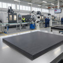Thick dark grey polyethylene slab on a factory floor, CNC machines and staff in blue behind