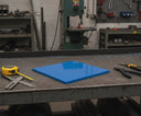 Blue polyethylene panel on a steel bench in front of a bandsaw, tape measure and snips beside it