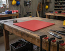 Red polyethylene panel on a worn timber bench in a workshop, clamps, knife and pliers around it