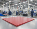 Large red polyethylene slab on a factory floor, workers in blue at machines in the background