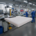 Thick white HDPE sheet on a conveyor in a bright factory, staff in blue overalls and a robot arm behind
