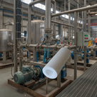 Opaque white PTFE tube composited over an industrial plant room with stainless vessels, pumps and pipework.