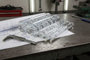 Clear bubble acrylic rods stacked over technical drawings on a bench, callipers alongside
