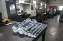 Stack of clear bubble acrylic rods on a bench in a workshop, CNC lathe and worker behind