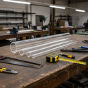 Clear acrylic tubes of graduated bores laid on a workshop bench beside a hacksaw, tape measure and pliers.