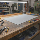 Off-white nylon panel on a timber workbench, milling machine and parts bins behind it