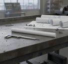 Natural white acetal rod on a workbench with rolled drawings and callipers by a window
