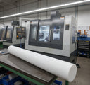 Large natural white acetal rod on a bench in front of a CNC machining centre