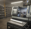 White acetal rod on a steel table in front of a grey CNC lathe in a tidy workshop