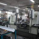 Pale grey PVC rod on a blue-framed bench in a workshop, CNC milling machine alongside