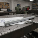 Grey PVC rod on a workbench over a wiring drawing with callipers, drill presses behind