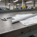 Grey PVC rod on a green-framed bench over a part drawing, vernier callipers alongside