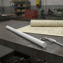 White polypropylene rod on a steel bench over yellowed drawings with callipers, lathes behind