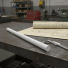 White polypropylene rod on a steel bench over yellowed drawings with callipers, lathes behind