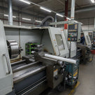 Natural white HDPE rod lying on a lathe bed in a busy workshop with an operator behind