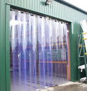 Clear PVC strip curtain hung in the doorway of a green clad workshop, photographed from outside