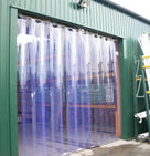 Clear PVC strip curtain hung in the doorway of a green clad workshop, photographed from outside
