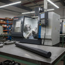 Black nylon rod on a steel table before a blue and white CNC lathe with swarf in its bed
