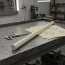Ivory nylon 6.6 rod on a steel bench across cream drawings, callipers and a pegboard behind