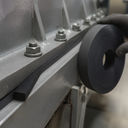 Gloved hand with a coil of thick black rubber strip beside a grey steel frame packed along its bolted seam