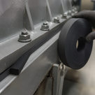 Gloved hand with a coil of thick black rubber strip beside a grey steel frame packed along its bolted seam