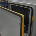 Open grey enclosure door with a black sponge rubber seal and yellow liner stripe around its inner edge