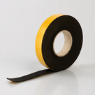 Narrow roll of black sponge rubber strip on a cardboard core, yellow liner on the side face, tail on the floor