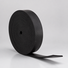 Thick black rubber strip coiled into a roll, standing upright with the tail sweeping out to one side