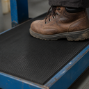 Brown leather work boot standing on fine fluted black rubber matting laid over a blue steel platform