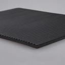 Black fluted rubber matting on a pale surface, fine parallel ribs running across the face with one corner lifted