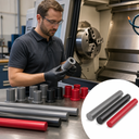 Machinist at a lathe checking a grey PVC bush, with grey, black and red rods and bushes on the bench