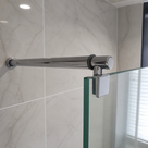 Round chrome support bar running from a marble-effect tiled wall to a glass shower panel, held by a square clamp.