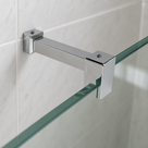 Square chrome bar spanning white tiles to a frameless glass screen, screwed clamp gripping the panel edge.