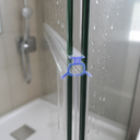 Lilac-tinted seal fitted at a shower door edge, bathroom shelf with bottles behind.