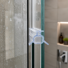 Clear winged seal clipped over the vertical edge of a shower door pane, tiled niche blurred behind