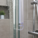 Clear hooked seal on the vertical edge of a wet shower panel, chrome bar valve on the tiled wall behind