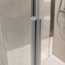 Clear I-beam seal fitted at a glass shower door hinge, niche shelf with a bottle behind.