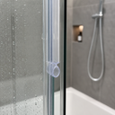 Clear ring-loop seal fitted to a glass shower door edge, shower head and hose behind.