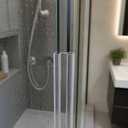 Two clear zigzag-top glass seals fitted at a bifold hinge, in a bathroom with shower and vanity.
