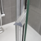 Clear wedge seal outlined in blue at a glass shower corner, grey tiles, white tray and chrome shower behind