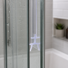 Clear cross-shaped seal on a glass panel upright, white tiled shelf with a potted plant and bath behind